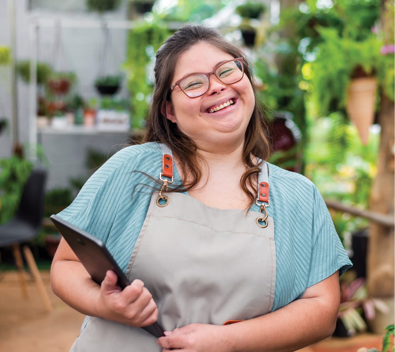 portrait of a smiling woman holding a clipboard with potted plants behind her